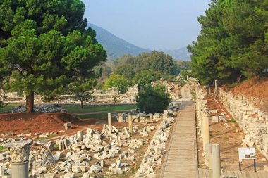 Efes antik kent kalıntılarında Ticari Agora boyunca ahşap bir geçit in yanında dağların ve mermer sütunların manzara görünümü, Türkiye'nin Selçuk kenti yakınında fotokopi alanı.