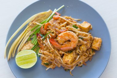 Kızarmış pirinç eriştesi (Pad Thai) karides, kızarmış tofu ve fasulye filizi ile karıştırılır. Limon ve muz çiçeğiyle süslenmiş mavi bir tabakta. Tayland Yemeği