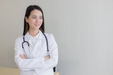 Siyah uzun saçlı Asyalı kadın doktor beyaz laboratuvar önlüğü ve steteskop takıyor. Hastanedeki ofisinde silah zoruyla duruyor..