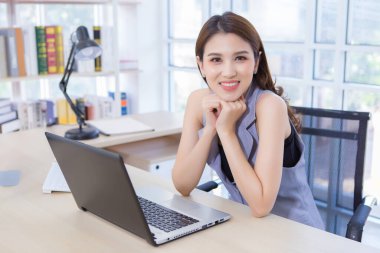 Evde oturup çalışan güzel bir kadın. Ev ofisindeki masaya dizilmiş bilgisayar ve lamba..