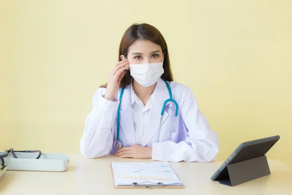 アジア系女性医師マスクを着用して診察室に座り 熟考します コロナウイルス保護の概念 — ストック写真