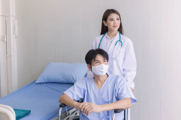 コロナウイルス保護の概念 病院で車椅子に座っている間に アジアの医師の女性は 彼の健康症状について顔マスクを着用男性患者と話しています — ストック写真