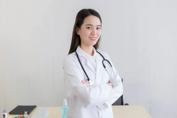 年轻美丽的亚洲女医生抱着胳膊高高兴兴地站在医院里 穿着白袍和听诊器 — 图库照片