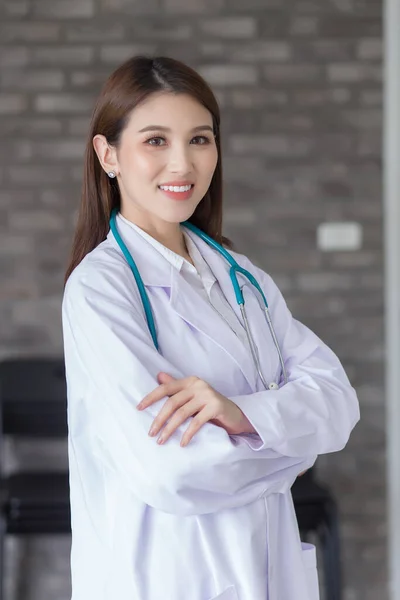 若い医師の女性が研究室のコートと聴診器を着て病院で腕を組んで — ストック写真