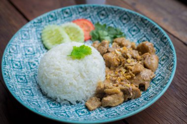 Pilav üzeri sarımsaklı ve biberli kızarmış tavuk mavi tabakta ve zemin olarak kahverengi ahşap..