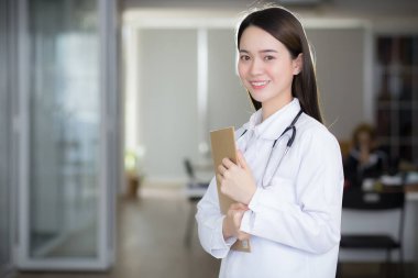 Asyalı doktor gülümsüyor ve elinde belge panosunu tutarken kendinden emin duruyor..