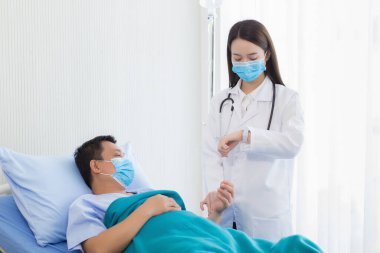 Asyalı bir kadın doktor hastanede kalp atışlarını kontrol etmek için hastanın bileğinin nabzını kontrol ediyor. Solunum sistemini (Covid-19) korumak için tıbbi yüz maskesi takarlar. Coronavirus koruma kavramı.