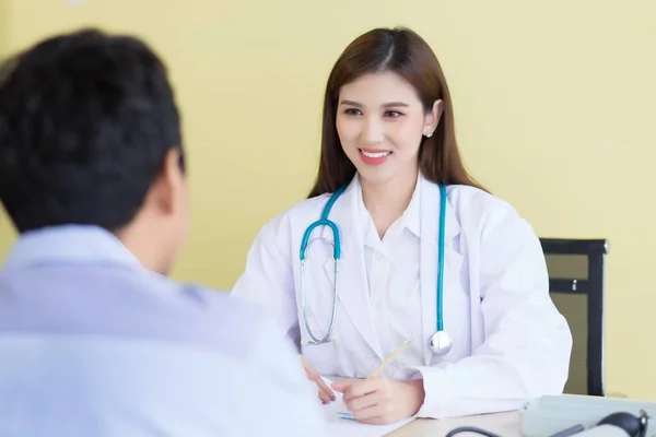 一位美丽的亚洲女医生笑着询问她的症状 穿着白色长袍和听诊器呆在医院 — 图库照片
