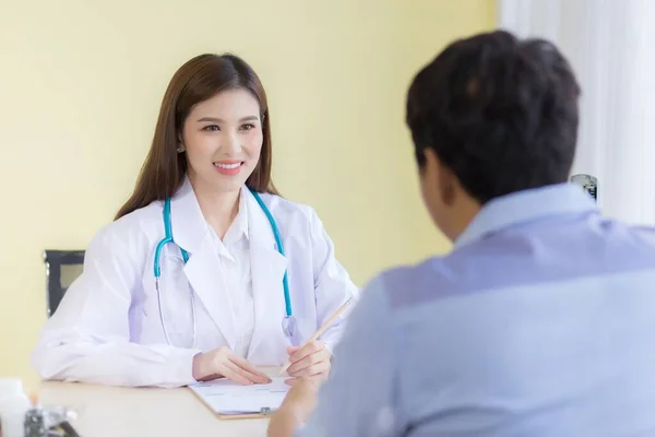 美しいアジアの女性医師が笑顔と症状について尋ねました 白い衣と聴診器を着たまま病院にいて — ストック写真