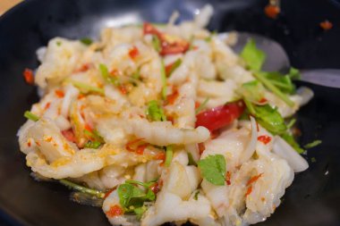 Baharatlı tavuk ayağı salatası otlarla karıştırılır ve siyah bir tabağa konur..