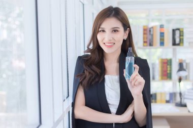 Ofisteki güzel bir bayan elinde alkol spreyi ile duruyor. Ofisin penceresinin yanında çeşitli patojenleri spreylemek için.