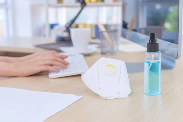 The portable alcohol spray and a N95 mask on the office desk. in the home office with a blurred background.