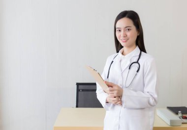 Hastanede çalışan genç, güzel Asyalı kadın doktor. Beyaz bir bornoz ve steteskop takıyor ve elinde bir pano tutuyor..
