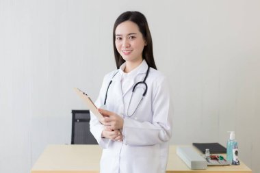 Hastanede çalışan genç, güzel Asyalı kadın doktor. Beyaz bir bornoz ve steteskop takıyor ve elinde bir pano tutuyor..