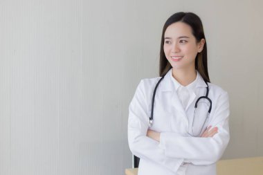 Siyah uzun saçlı Asyalı kadın doktor beyaz laboratuvar önlüğü ve steteskop takıyor. Hastanedeki ofisinde silah zoruyla duruyor..