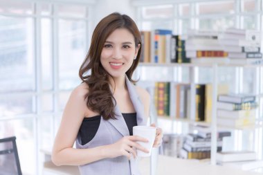 Güzel bir kadın evde çalışırken elinde beyaz bir bardak tutuyor..