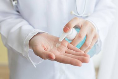 Kadın doktor, hastalık muayenesini beklerken ellerini yıkamak için alkol jeli kullanarak oturdu..