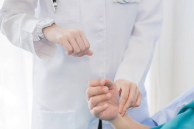 Bir kadın doktor, hastanede kalp atışlarını kontrol etmek için hastanın bileğinin nabzını kontrol ediyor.. 