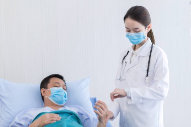 Asyalı bir kadın doktor hastanede kalp atışlarını kontrol etmek için hastanın bileğinin nabzını kontrol ediyor. Solunum sistemini (Covid-19) korumak için tıbbi yüz maskesi takarlar. Coronavirus koruma kavramı.