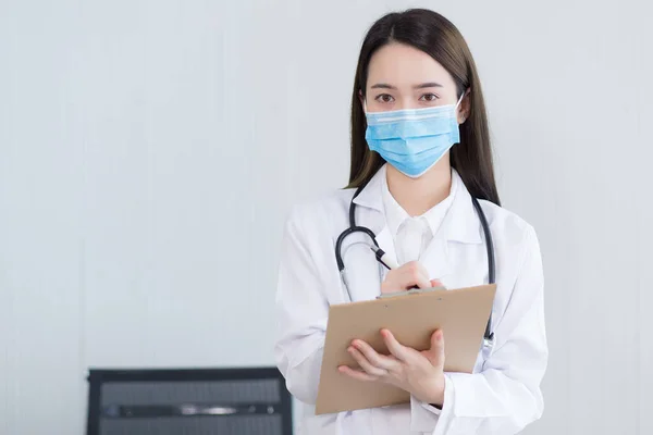 アジアの女性医師は 医療面マスクを着用し コヴィド19でクリップボードに彼女の患者の症状を記録 コロナウイルス 保護コンセプト — ストック写真