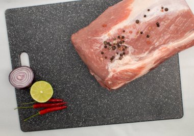 Baharatlı ve sebzeli mermer bir tahtanın üzerinde çiğ domuz eti.