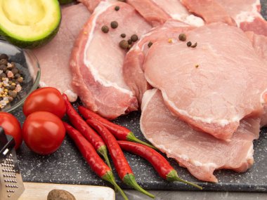 Baharat ve sebzelerle mermer bir tahtada çiğ domuz bifteği.