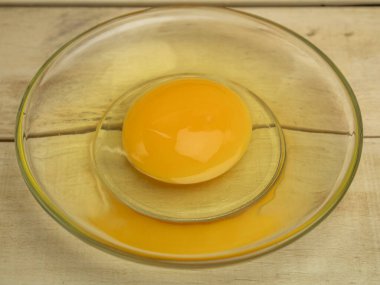 Ahşap arka planda cam bir tabakta kırılmış tavuk yumurtası.