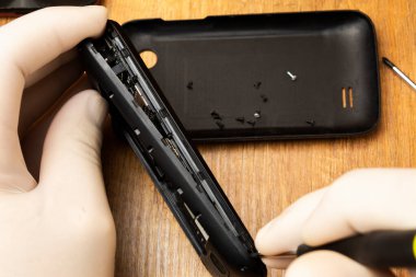 Elinde tornavida olan usta masanın üzerinde bir cep telefonunu söker.