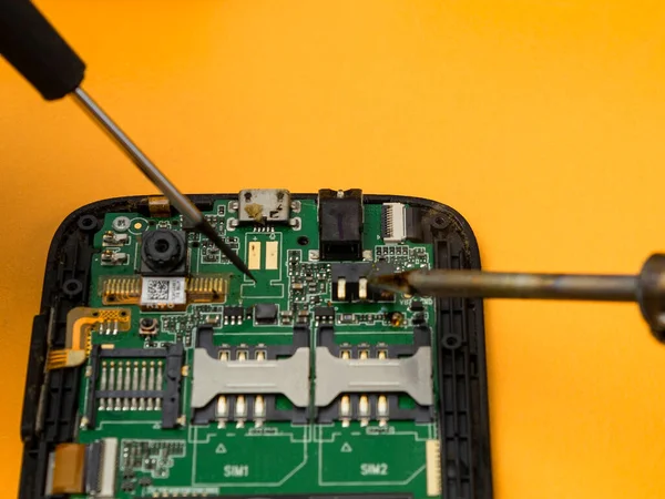 Cep telefonunu lehim makinesi ve tornavidayla tamir etmek.