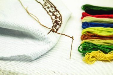 İğne ve beyaz kumaşlı nakış işlemek için çok renkli iplikler. Beyaz bir kumaşa iğne batırılmış nakış iplikleri..