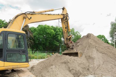 Bir kazıcı bir kovada zemin kazıyor. Turuncu ve kürekle kazıcı