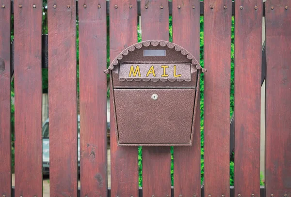 A mail box hangs on a fence. Mailbox on a wooden fence