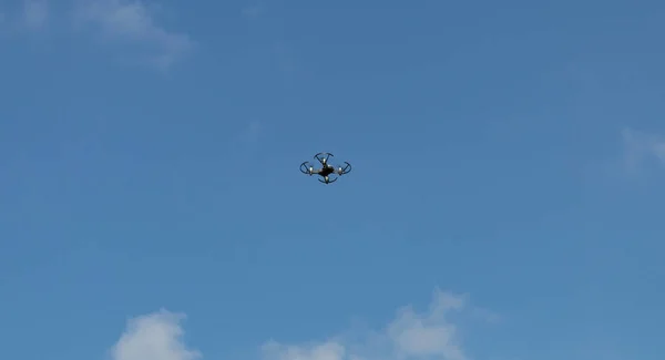 Drone in flight above the crowns of trees. Photo of a flying drone on a background of blue sky and white clouds. Drone is watching