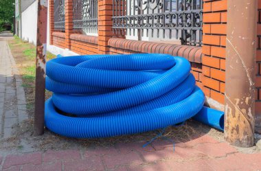 Oluklu boru rulo şeklinde bükülmüş. Mavi kıvrımlı boru yerde yatıyor.