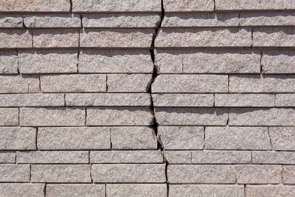A large crack in the wall of granite slabs. Cracked wall