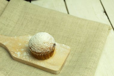 Metnin arka planı olarak küçük bir panoda kek. Kağıt kalıpta bir kek ve üzerine pudra şekeri serpilmiş.