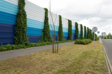 Noise fence on city roads. Climbing plant on the fence of the noise barrier and in the background - residential buildings clipart