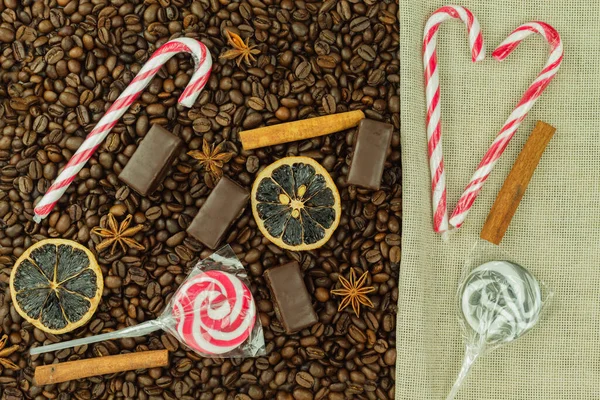 Chocolate candies and roasted coffee beans as a background. Red-white lollipops and chocolate candies on the background of coffee beans and place for text. Wallpaper for menu or flyer