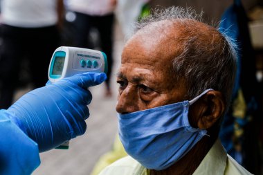 Mumbai, Hindistan / 17 Haziran 2020: Bir sağlık çalışanı Corona virüs tarama kampı sırasında Ghatkopar East 'teki Ramabai Ambedkar Nagar' ın varoşlarında yaşayan birinin sıcaklığını kontrol ediyor