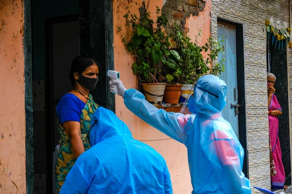 Mumbai, Hindistan / 17 Haziran 2020: Bir Corona virüs tarama kampı sırasında Ghatkopar East 'teki Ramabai Ambedkar Nagar' ın varoşlarındaki sakinlerin sıcaklıklarını kontrol ederken sağlık çalışanları Kişisel Koruyucu Ekipman (PPE) takıyorlar.