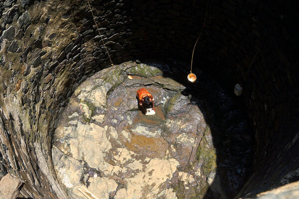 Махараштра, Индия / 6 мая 2016 года: Мальчик спускается по глубокому колодцу, чтобы принести воду из почти сухого колодца в деревне Дхакне, Шахапур Талука, район Тане
