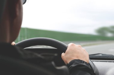 Otoyol bulanık bir arka planda bir otomobilin direksiyon simidi üzerinde erkek ellerde yakın çekim (azaltılmış ton etkisi)