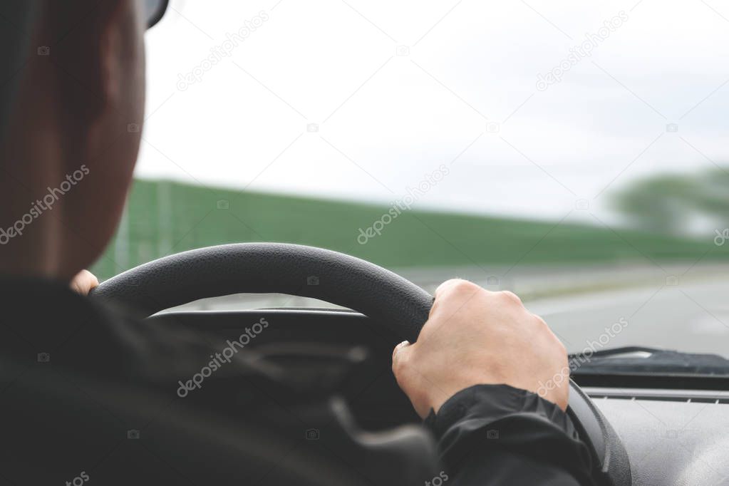 Close-up on male hands on the steering wheel of a car on a blurred background of the highway (reduced tone effect)
