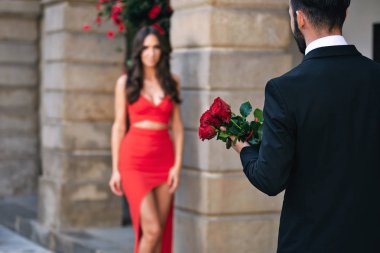 Arkadan görünüşü romantik kalma sırasında bir kadın için bir buket kırmızı gül veren bir adam.
