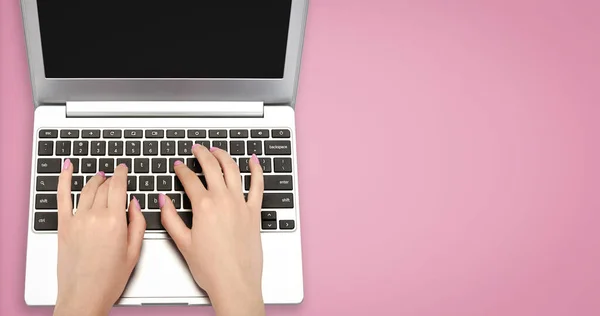 Üst görüntüde mükemmel kadın elleri pembe arka planda bir dizüstü bilgisayarda fotokopi alanı ile yazı yazıyor.