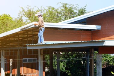 İşçiler çatılar inşa ediyor. O da çatıda duruyordu..