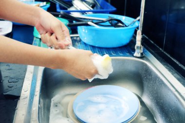 Kadının eli bulaşık çatalı ve kaşığı lavaboyla yıkıyor..