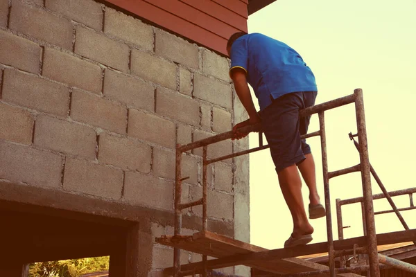 İşçi bir ev yapmak için iskeleye tırmanıyor.
