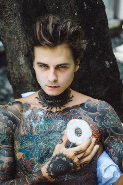 Genç yakışıklı adam açık havada bahçede açık havada yatakta kahvaltı dövme