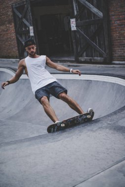 Bir havuzda pateni bir şık genç adam bir skatepark, bir kaykay üzerinde beyaz bir T-shirt ve şapka paten.